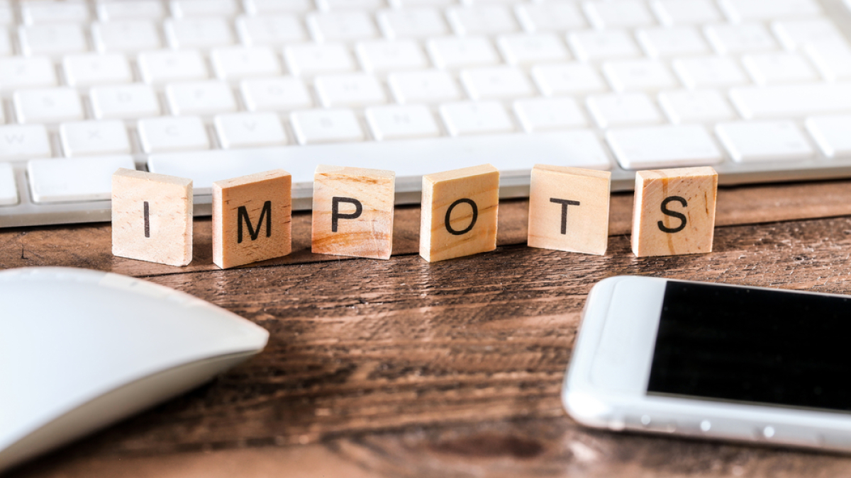 Il existe plusieurs dispositifs de défiscalisation permettant aux investisseurs de réduire leurs impôts Investissement locatif Montpellier –Lettres en bois inscrivant le mot impôts sur un bureau à côté d’un clavier d’ordinateur et d’un téléphone