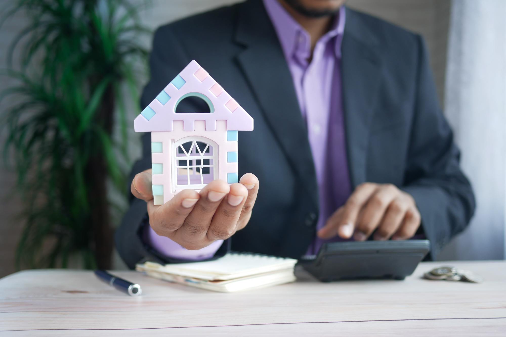 Homme en costard tenant une maison dans sa main