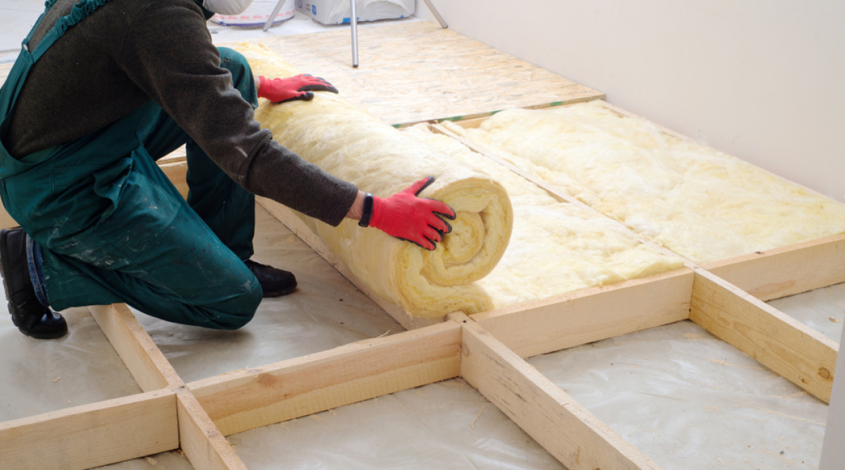 Il est important d’encourager les propriétaires à réaliser des travaux de rénovation énergétique assouplissement interdiction location passoire thermique – Un ouvrier isole le plancher d'une maison avec de laine de verre