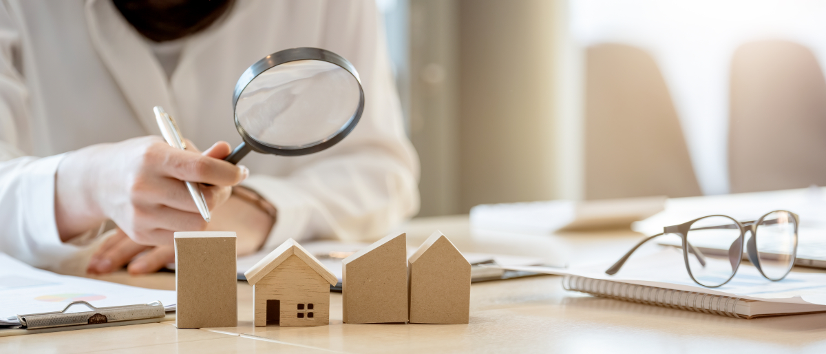Nouveau zonage loi Pinel 2022 – Une personne tient une loupe dans sa main et observe une petite maison en bois sur son bureau