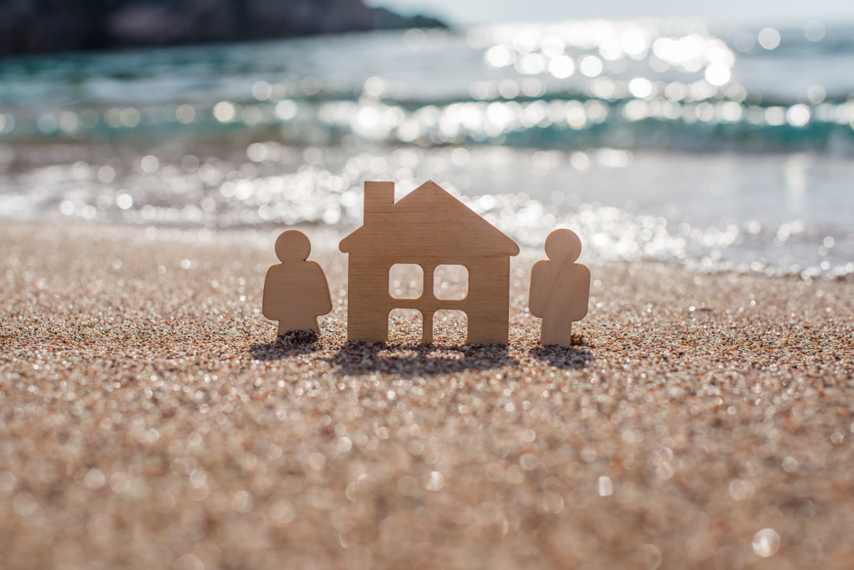 Figurines en bois d’une maison et d’un couple posées sur une plage