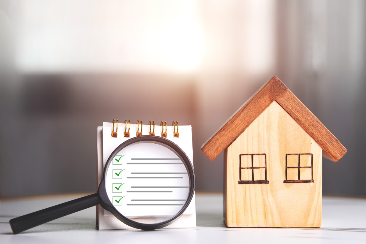 Des critères spécifiques sont observés lors des inspections pour le permis de louer permis de louer montpellier – Une loupe pointée sur une "checklist" à côté d'une maison miniature en bois