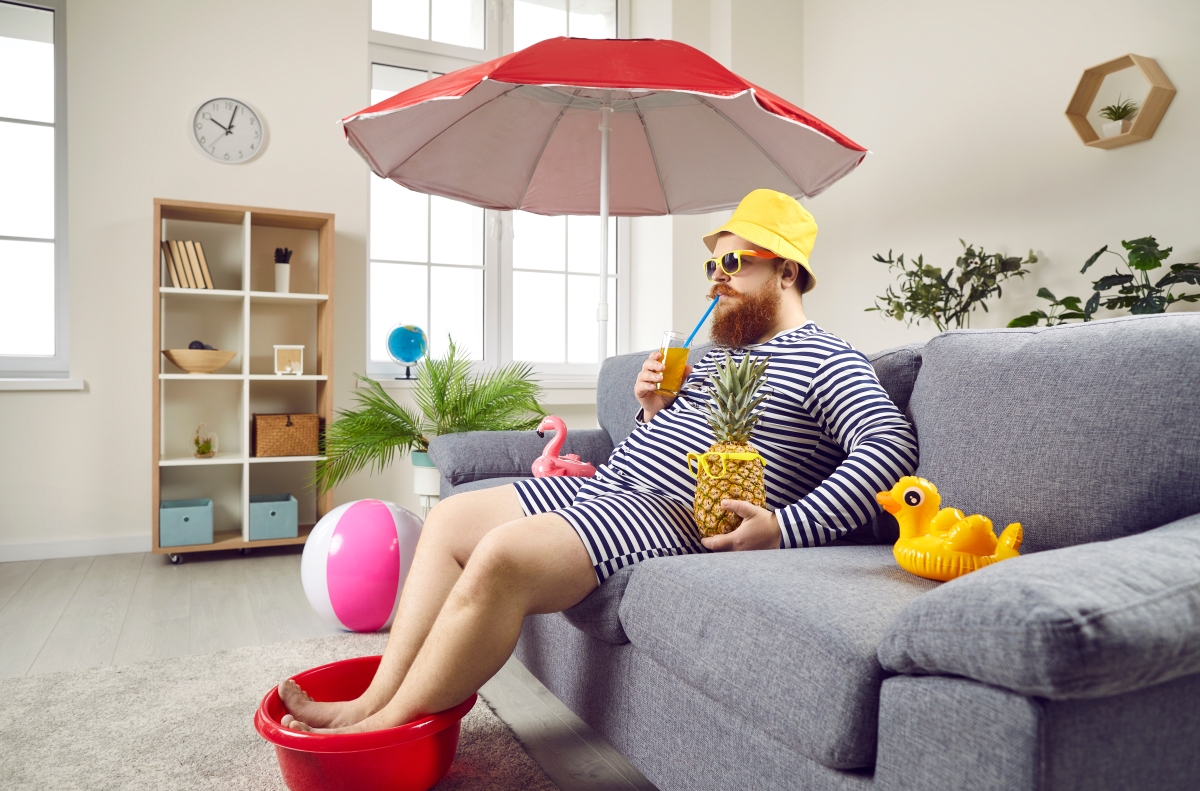 location saisonniere vs meublé de tourisme – un homme sirote un verre avec une paille sous un parasol avec un ananas et un canard de bain, au milieu de son salon 