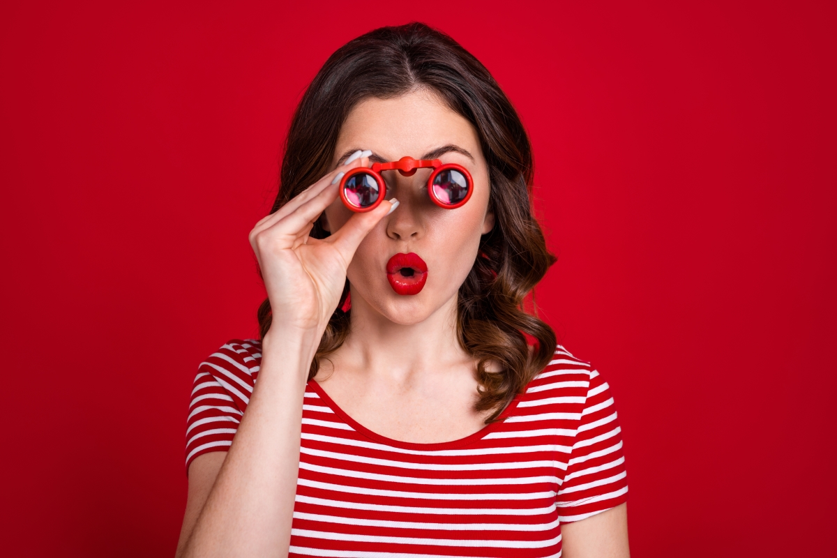 les fins de programmes, soldes et opérations de déstockages sont l’occasion d’acheter neuf à prix réduit. une femme avec des jumelles rouges, du rouge à lèvres rouge sur fond rouge