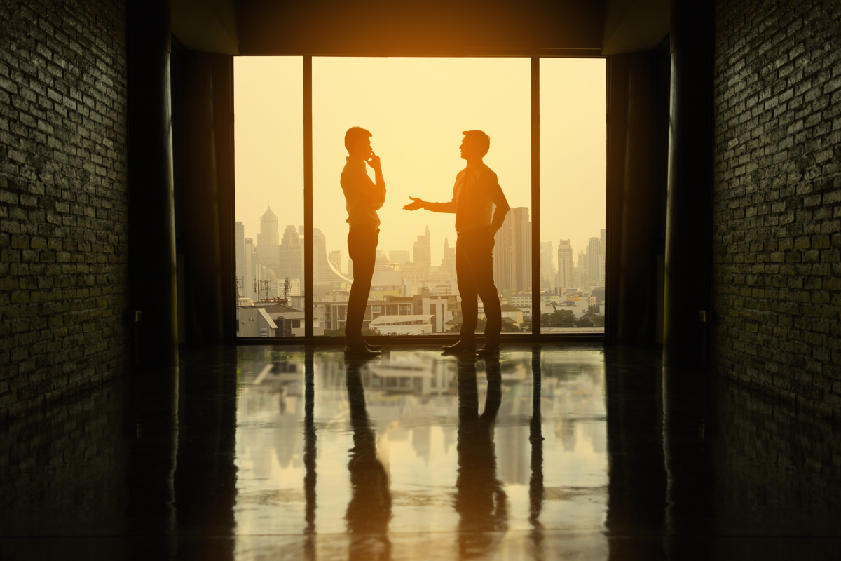 deux hommes dans un bureaux négocient devant une vue d’une grande ville au coucher du soleil