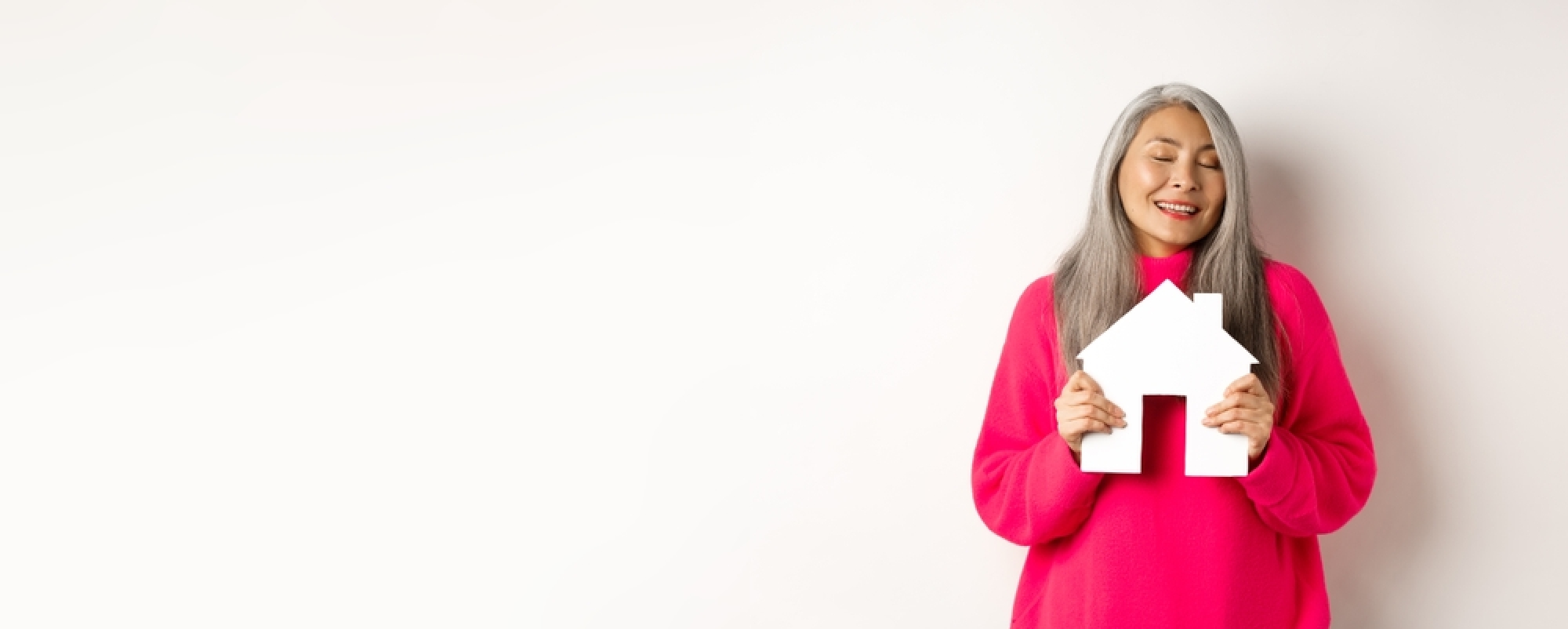une femme en pull rose tient une petite maison en souriant