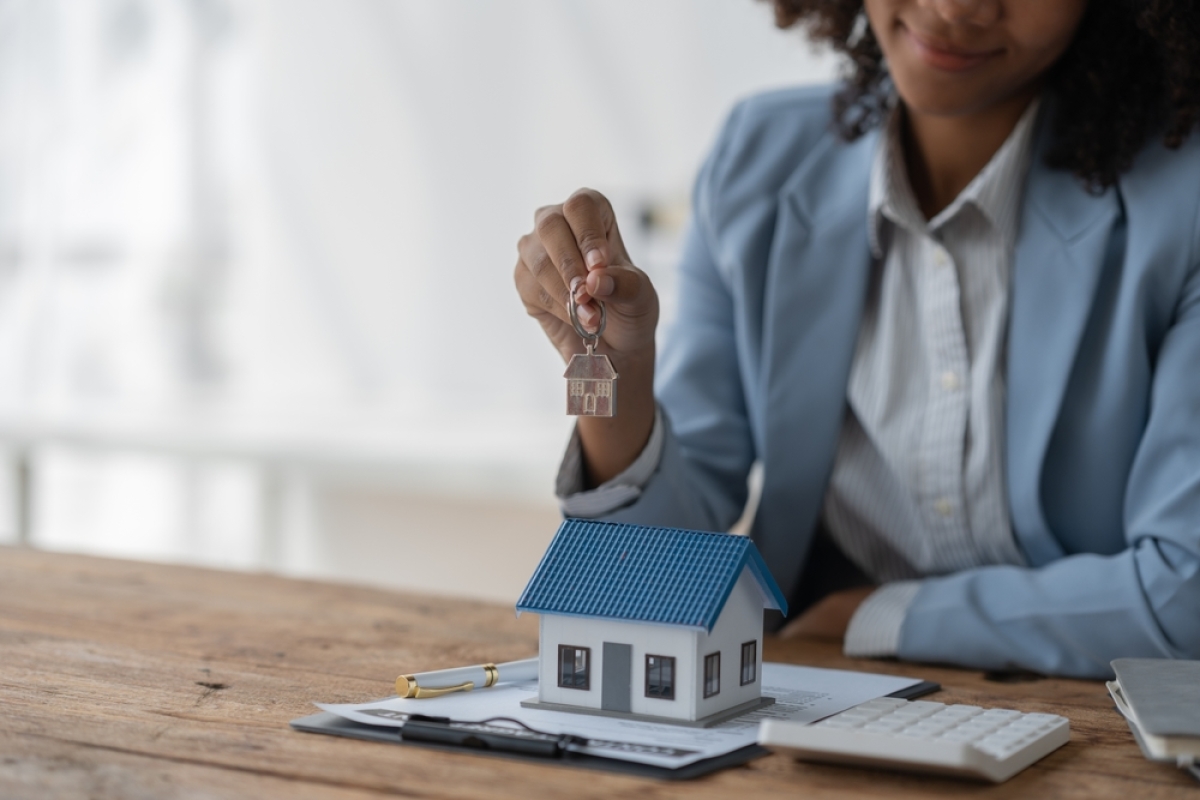 gestion locative saisonnière – une femme tient une clé au-dessus d'une maquette de maison 