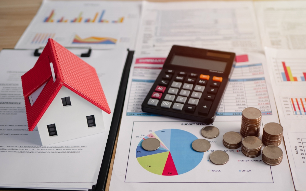 La LTV et la THLV ont des conditions d’application différentes taxe logements vacants – maquette de maison calculatrice et tas de pièces au dessus de documents de calcul