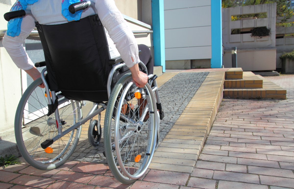normes PMR immobilier neuf – Une personne en fauteuil roulant emprunte une rampe d’accessibilité