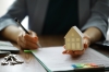 un homme signe un dossier d'une main et tient une maquette de maison de l'autre